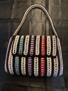 a multicolored handbag sitting on top of a black cloth covered tablecloth