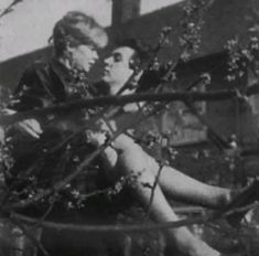 black and white photograph of two people sitting on the ground in front of a tree