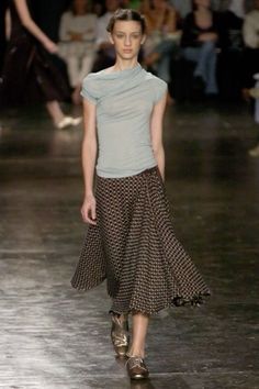 a woman is walking down the runway wearing a skirt and t - shirt with an asymmetrical design