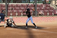 a batter, catcher and umpire during a baseball game on a dirt field with bleachers in the background