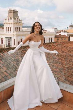 a woman standing on top of a roof with her arms outstretched in the air and wearing a white dress