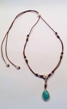 a necklace with a turquoise stone and pearl beads on a brown cord that is attached to a white background