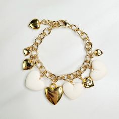 Vintage hearts are the focal point of this love filled bracelet. An assortment of gold plated hearts and matte ivory hearts play along the edge, perfect as a gift for someone you love. Handmade in the United States, a matching necklace and earring set are available. Features: - Gold Plated Vintage Hearts - Matte Ivory Vintage Hearts - Gold Plated Mixed Cable Chain - Lobster Claw Clasp - Extension - Handmade in the United States Dimensions: - Length: 7.5" - Extension: 1" - Total Length: 8.5" Heart-shaped Jewelry With Dangling Charms For Valentine's Day, Heart-shaped Dangling Charms Jewelry For Valentine's Day, Gold Metal Charm Bracelet With Heart Beads, Metal Heart Beads Jewelry For Anniversary, White Jewelry With Adjustable Chain For Valentine's Day, Gold-tone Metal Jewelry With Heart Charm, Valentine's Day Gold-plated Jewelry With Dangling Charms, White Heart-shaped Metal Charm Bracelet, White Dainty Metal Charm Bracelet