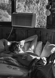 a shirtless man laying on top of a bed next to an air conditioner