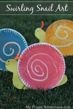 three paper plates with snails on them sitting in the grass, and one is painted red