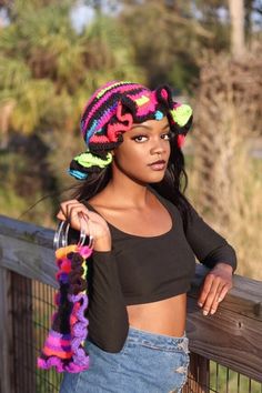 a woman wearing a colorful knitted hat leaning on a wooden fence with her hand in her pocket