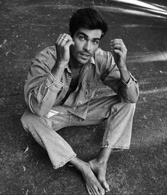 a young man sitting on the ground with his hands in his hair and looking at the camera