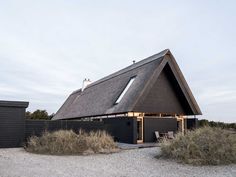 a black house with a thatched roof on gravel ground next to grass and bushes