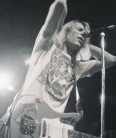 a man with long hair playing an electric guitar in front of a microphone on stage