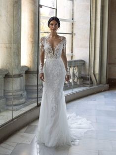 a woman in a white wedding dress standing by a window