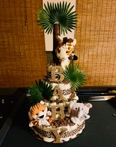 a three tiered cake with animals and palm trees on the top, in front of bamboo blinds