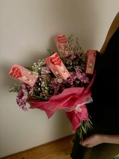 a woman holding a bouquet of flowers with pink and white ribbons on it's side