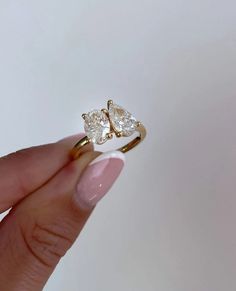 a woman's hand holding a gold ring with two pear shaped diamonds