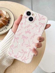 a person holding up a phone case with pink bows on it and a donut in the background