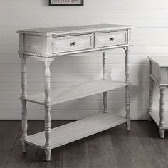 a white table with two drawers next to a wooden shelf on the floor in front of a wall