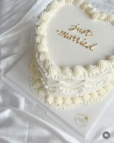 a heart shaped cake with the words first married on it sitting on a white sheet