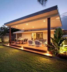 an outdoor living area with lights on the roof and chairs in the grass at night