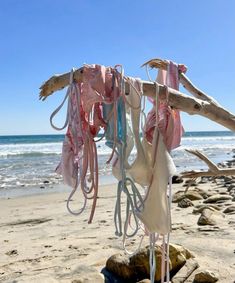 several pieces of cloth hanging from a tree branch on the beach with waves in the background