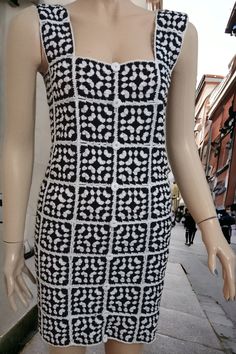 a mannequin wearing a black and white dress on a sidewalk with buildings in the background