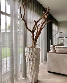 a tall vase with branches in it sitting next to a window covered by sheer curtains