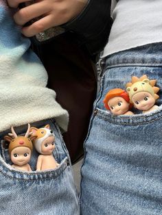 two children's dolls are in the pocket of their jeans, one is holding a cell phone