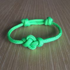 a close up of a green rope bracelet on a wooden table with a knot at the end