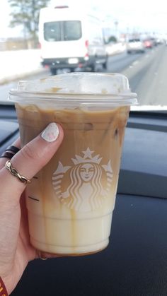 a hand holding up a cup of coffee in front of a car window with traffic on the road behind it