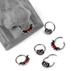 four pairs of cat nose rings with red eyes and fangs on the end, sitting next to a rock