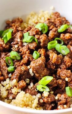 a white bowl filled with meat and rice on top of a wooden table next to a fork