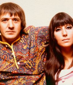 two people sitting next to each other with long hair and wearing colorful clothing, one person is looking at the camera