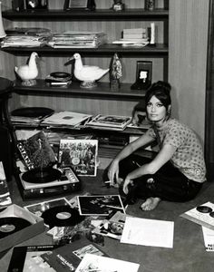 a woman sitting on the floor in front of a record player surrounded by records and cds