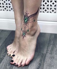 a woman's foot with a green and black tattoo design on her left leg