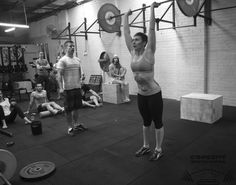 a woman lifting a barbell in a crossfit gym with other people watching