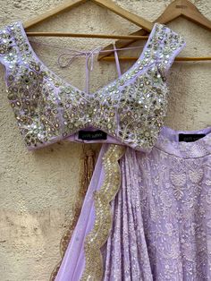 A three-piece lavender lucknowi mirror lehenga set from the Priti Sahni collection. This elegant lavender georgette lehenga with heavy gota, sequins, pearl and zari work border is paired with lavender blouse in raw silk fabric with mirror, pearl and zardozi hand work embroidery. The lehenga has side hanging ball tassels to the waistline. And the blouse has a sequins tassel tie-up at the back. The outfit is completed with a lavender mirror net dupatta with scalloped edging. Designer Purple Choli With Gota Work, Traditional Drape Lavender Choli For Wedding, Lavender Choli With Dupatta In Traditional Drape, Designer Lavender Sharara With Zari Work, Lavender Sets With Zari Work In Traditional Drape, Elegant Lavender Sharara With Zari Work, Lavender Sharara With Intricate Embroidery For Wedding, Lavender Embroidered Sharara For Wedding, Bollywood Style Lavender Sharara With Mirror Work