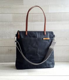 a black bag sitting on top of a white table next to a wooden wall with a brown leather handle