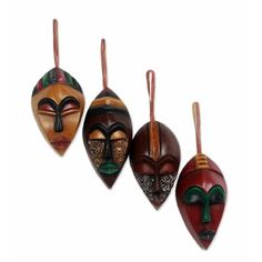 three wooden masks hanging from strings on a white background, each with different designs and colors