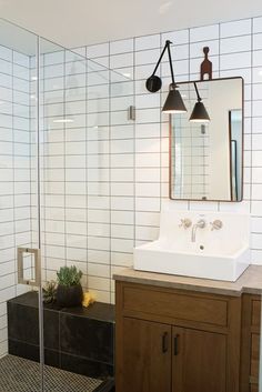 a white sink sitting under a mirror next to a walk in shower and wooden cabinet