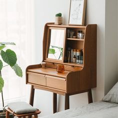 a wooden desk with a mirror on it next to a plant in a vase and a stool