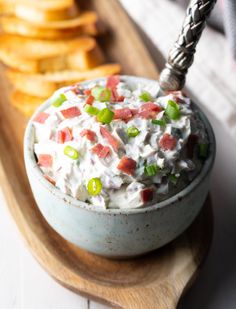 a bowl of potato salad on a wooden platter with crackers and a fork