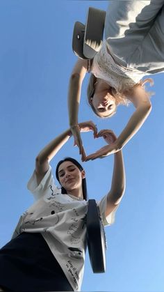 two women making a heart shape with their hands while standing in front of a blue sky