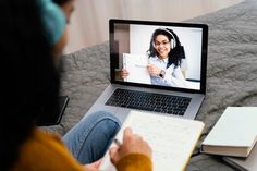 a person sitting on a bed with a laptop and notebook in front of their face