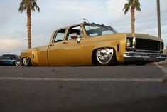 an old yellow pickup truck parked in a parking lot with palm trees and other cars