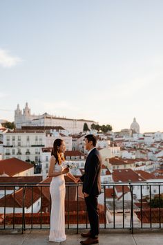 a man and woman standing next to each other on top of a roof looking at each other