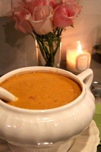 a white bowl filled with soup on top of a table next to candles and flowers