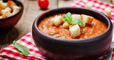 a bowl of tomato soup with bread croutons and basil leaves on the side