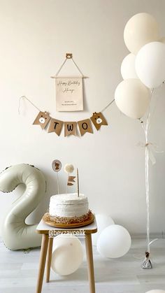 a birthday cake sitting on top of a wooden table next to balloons and streamers