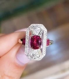 a close up of a person holding a ring with a red and white stone in it