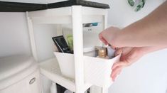 a person holding a container in front of a bathroom sink with the door open and shelving underneath it