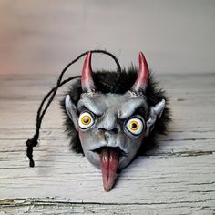 a creepy mask with horns and big yellow eyes on a wooden surface, showing its tongue out