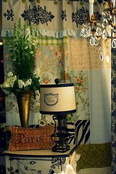 there is a lamp and some flowers on top of a table in front of a curtain